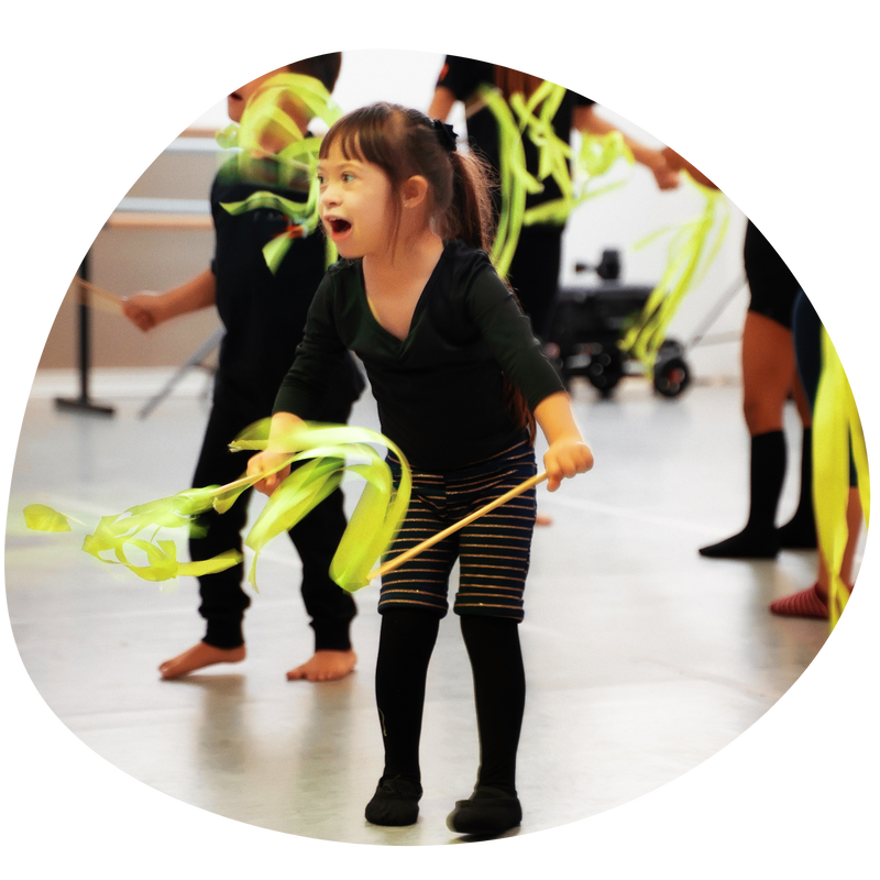 child appears to be participating in a dance class, holds yellow ribbon and wears black leotard