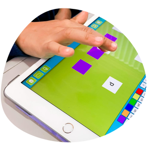 ID: An iPad is flat on a desk, on the screen: a website with black and white alphabet letter tiles at the top with a blue background, the letters' s', 'i', 'p', and three purple squares can be seen on a green background underneath the alphabet tiles. A child's hand can be seen in the top left corner, dragging down a letter with their finger to the second purple square. Picture